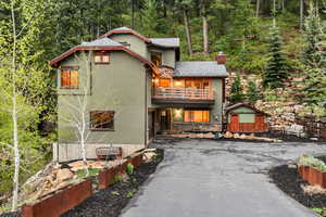Rear view of property with a balcony, driveway, stucco siding, a chimney, and a wooded view