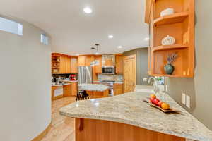 Kitchen featuring open shelves, stainless steel appliances, a sink, light wood finished floors, and decorative backsplash