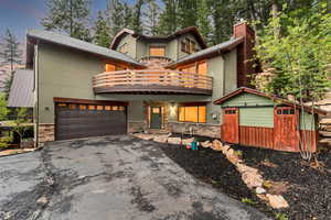 View of front of home with a balcony, stone siding, stucco siding, and driveway