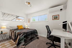 Carpeted bedroom with a wall mounted AC, baseboards, and a desk