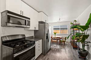 Kitchen featuring appliances with stainless steel finishes, dark wood-style floors, dark countertops, white cabinets, and baseboards
