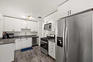 Kitchen featuring appliances with stainless steel finishes, a sink, dark countertops, dark wood-style flooring, and white cabinetry