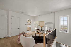 Living room with light wood-style flooring, a textured ceiling, arched walkways, and baseboards