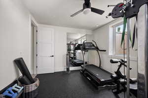 Exercise room with ceiling fan, a textured ceiling, and baseboards