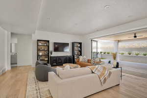 Living area with a textured ceiling, light wood-style flooring, and baseboards