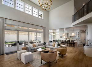 Living room with a chandelier, a high ceiling, light wood-style floors, and healthy amount of natural light