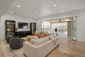 Living room with light wood-type flooring, a textured ceiling, recessed lighting, baseboards, and ceiling fan