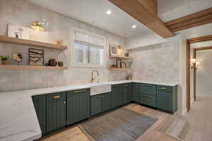 Kitchen with green cabinets, open shelves, a sink, decorative backsplash, and light stone countertops