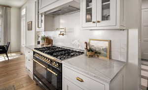Kitchen with range with two ovens, white cabinetry, light wood-style floors, and glass insert cabinets