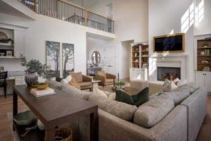 Living room with a towering ceiling, wood finished floors, a warm lit fireplace, baseboards, and built in shelves