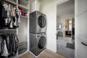 Washroom with stacked washer / drying machine, light wood-style floors, and baseboards