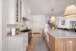 Kitchen featuring stainless steel range, a sink, premium range hood, light wood-style flooring, and glass insert cabinets