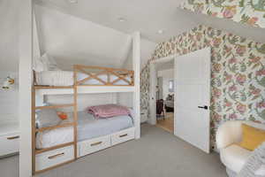 Carpeted bedroom with vaulted ceiling and wallpapered walls