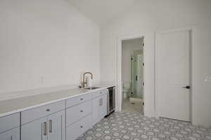 Kitchen featuring beverage cooler, a sink, vaulted ceiling, gray cabinetry, and light countertops