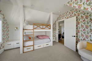 Bedroom featuring wallpapered walls, vaulted ceiling, and light colored carpet