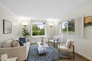 Formal living room with crown molding, wainscot detail, hardwood floors, fresh paint, bay box window, and plantation shutters