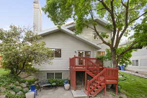 View of the back of the home with deck, stairs, shade tree, and first patio