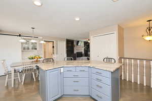 Kitchen with decorative light fixtures, a brick fireplace, light stone counters, recessed lighting, and a center island