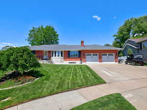 Single story home featuring brick siding, an attached garage, driveway, a chimney, and a front lawn