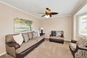 Living area featuring ornamental molding, carpet, baseboards, and a ceiling fan