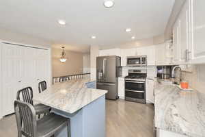 Kitchen featuring appliances with stainless steel finishes, a sink, a kitchen breakfast bar, white cabinetry, and backsplash