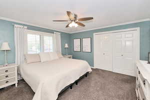 Bedroom with dark carpet, a closet, crown molding, and ceiling fan
