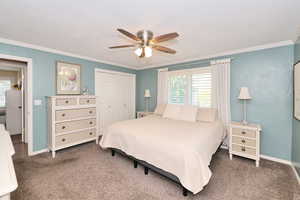 Carpeted bedroom featuring ornamental molding, a closet, baseboards, and ceiling fan