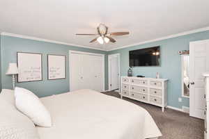 Bedroom featuring ornamental molding, dark carpet, a closet, a ceiling fan, and baseboards