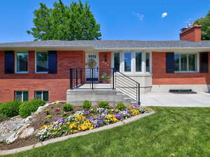 View of front facade featuring a front yard, brick siding, a shingled roof, and a chimney