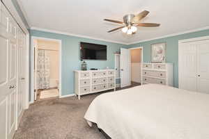 Carpeted bedroom featuring ornamental molding, ensuite bath, ceiling fan, baseboards, and a closet