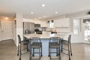 Kitchen with appliances with stainless steel finishes, white cabinets, a sink, light stone countertops, and a breakfast bar
