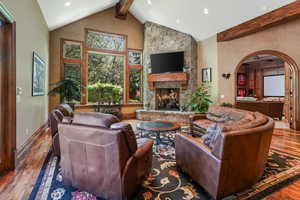 Living room with hardwood / wood-style flooring, beamed ceiling, a stone fireplace, recessed lighting, and high vaulted ceiling