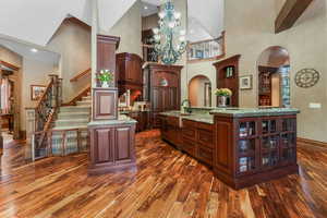 Bar with arched walkways, dark wood-style flooring, high vaulted ceiling, baseboards, and a sink