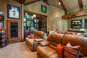 Cinema room featuring beam ceiling, high vaulted ceiling, light colored carpet, and bar