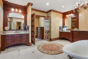 Full bathroom with ornamental molding, baseboards, a freestanding bath, two vanities, and recessed lighting