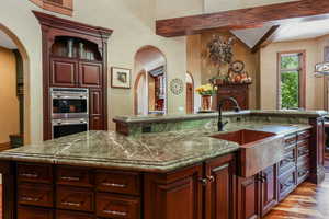 Kitchen featuring arched walkways, a sink, double oven, an island with sink, and light wood finished floors