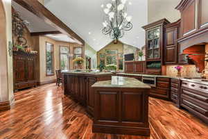Kitchen with a chandelier, an island with sink, dark wood-style floors, decorative light fixtures, and glass insert cabinets