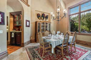 Dining room with baseboards, a towering ceiling, arched walkways, a chandelier, and bar