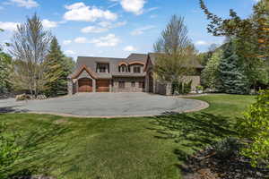 View of front of property with stone siding, driveway, a front yard, and a garage with large parking pad