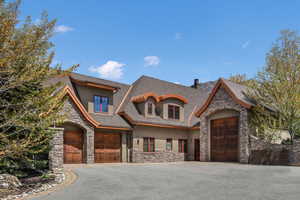 View of front of property with stone siding, stucco siding, asphalt driveway, roof with shingles, and a chimney