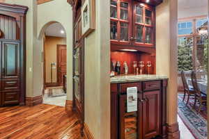 Indoor dry bar featuring wine cooler, arched walkways, light wood-style floors, baseboards, and a towering ceiling