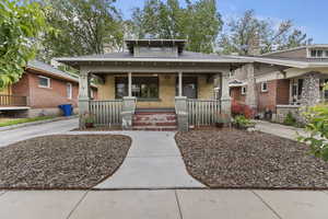 View of front of property featuring a porch, brick siding, a chimney, and a shingled roof