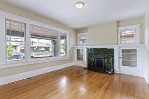 Living room with plenty of natural light, wood finished floors, a tiled fireplace, and baseboards
