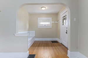 Foyer entrance with arched walkways, light wood-style floors, and baseboards