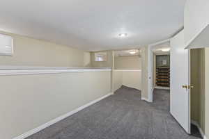 Finished basement featuring dark carpet, a textured ceiling, stairway, and baseboards