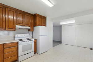 Kitchen featuring white appliances, under cabinet range hood, light flooring, and brown cabinets