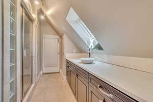 Bar with a skylight, a sink, lofted ceiling, light tile patterned floors, and baseboards