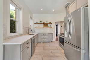 Kitchen featuring stainless steel appliances, open shelves, a sink, gray cabinets, and backsplash