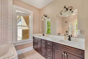 Bathroom featuring healthy amount of natural light, tiled shower, a tub, and double vanity