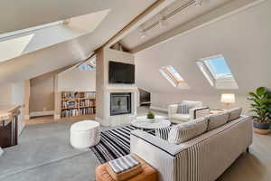Living area featuring a skylight, a tile fireplace, lofted ceiling, rail lighting, and baseboards